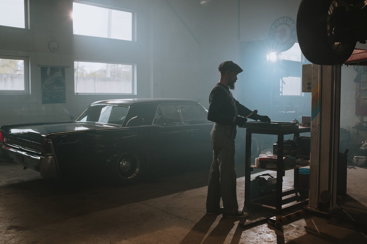 A mechanic working on a classic car in a dimly lit garage, showcasing vintage automotive repair.